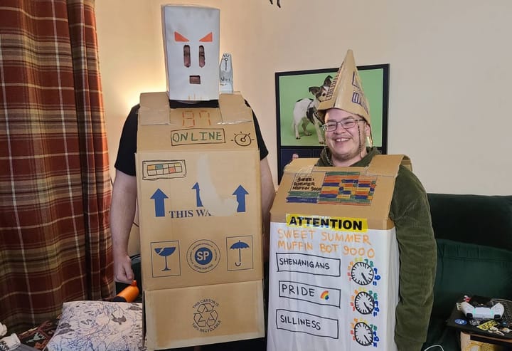 A taller man and a shorter man both dressed like robots in cardboard boxes. Controls read "shenanigans", "pride", "sillyness".