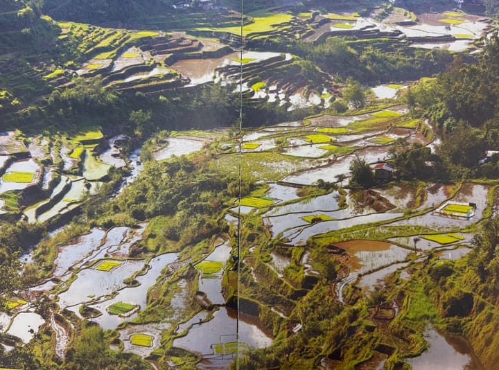 A sweeping aerial shot of hundreds of green flooded rice terraces down a set of mountains